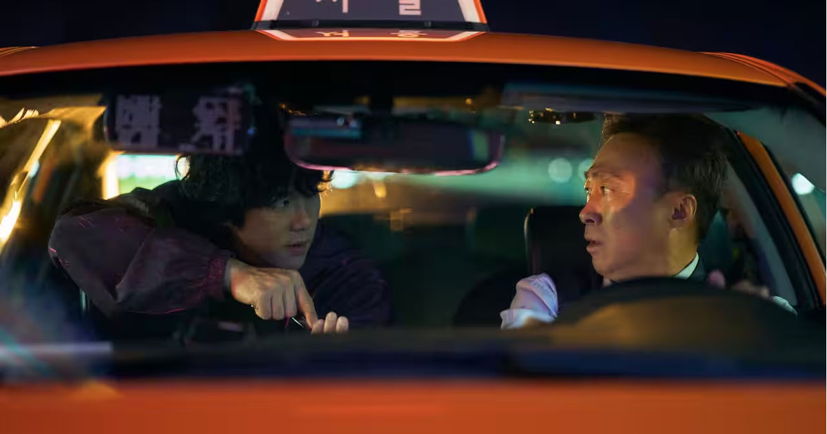 A scene from A Bloody Lucky Day showing Lee Sung-min driving a yellow taxi, with Yoo Yeon-seok as his passenger.